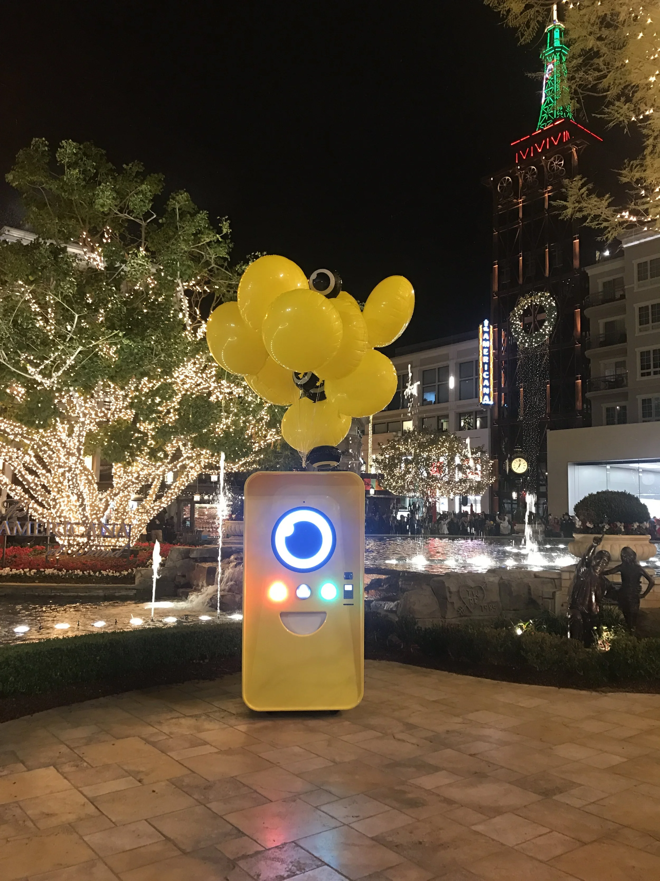 Yellow Snapbot Spectacles vending machine with balloon bunch at a lit outdoor plaza at night